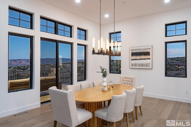 dining room with light wood-type flooring, a mountain view, a towering ceiling, and a chandelier