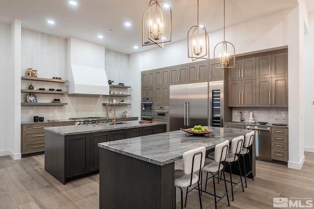 kitchen featuring a kitchen island with sink, sink, a notable chandelier, appliances with stainless steel finishes, and decorative light fixtures