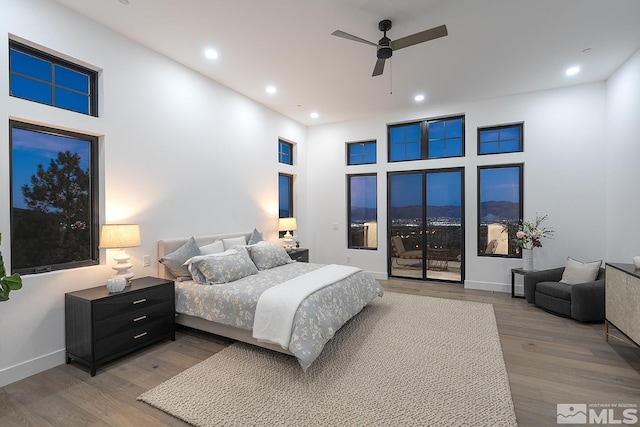 bedroom with wood-type flooring, a high ceiling, access to outside, and ceiling fan