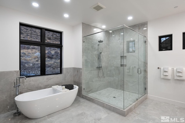 bathroom with shower with separate bathtub and tile walls