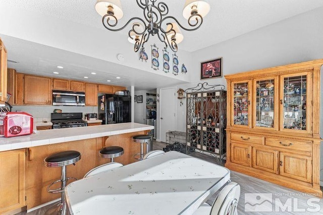 interior space featuring light wood-type flooring, a kitchen breakfast bar, an inviting chandelier, black appliances, and tile countertops