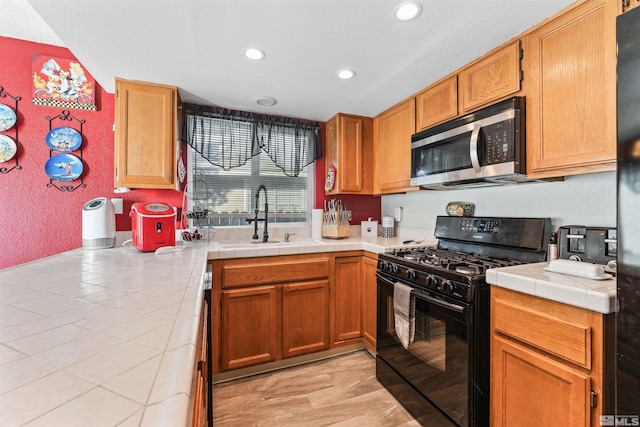 kitchen with tile counters, sink, and black gas range