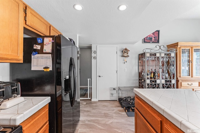 kitchen featuring black appliances, a textured ceiling, and tile countertops