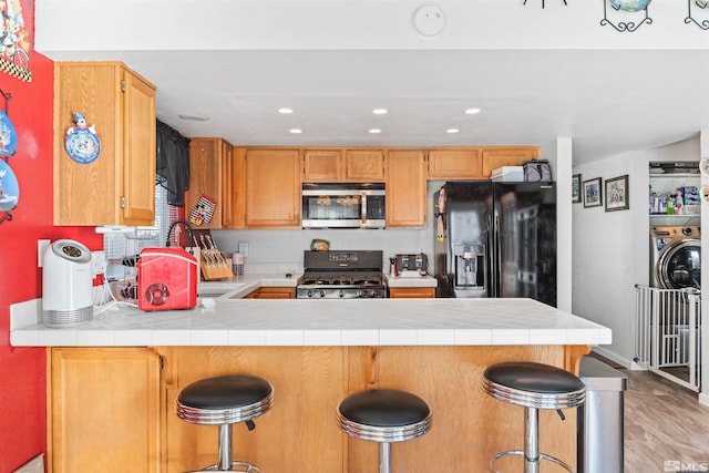 kitchen featuring light wood-type flooring, black appliances, kitchen peninsula, and a kitchen bar