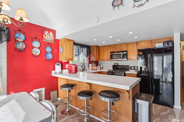 kitchen with vaulted ceiling, kitchen peninsula, tile countertops, black appliances, and hardwood / wood-style flooring