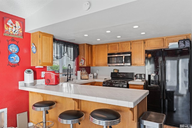 kitchen featuring black appliances, kitchen peninsula, tile countertops, and a breakfast bar area