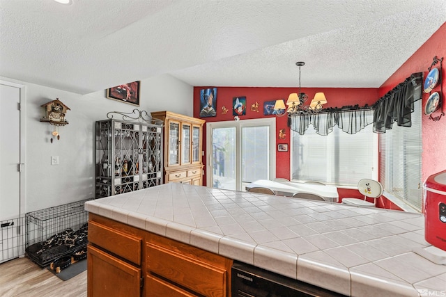 kitchen with tile countertops, light wood-type flooring, lofted ceiling, decorative light fixtures, and a notable chandelier