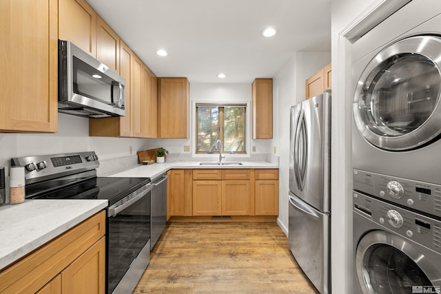 kitchen with light wood-type flooring, sink, stacked washing maching and dryer, stainless steel appliances, and light brown cabinets