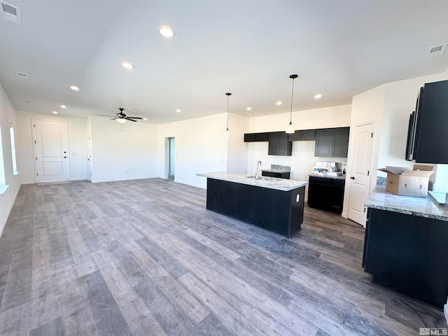 kitchen with dark wood-type flooring, sink, hanging light fixtures, ceiling fan, and an island with sink