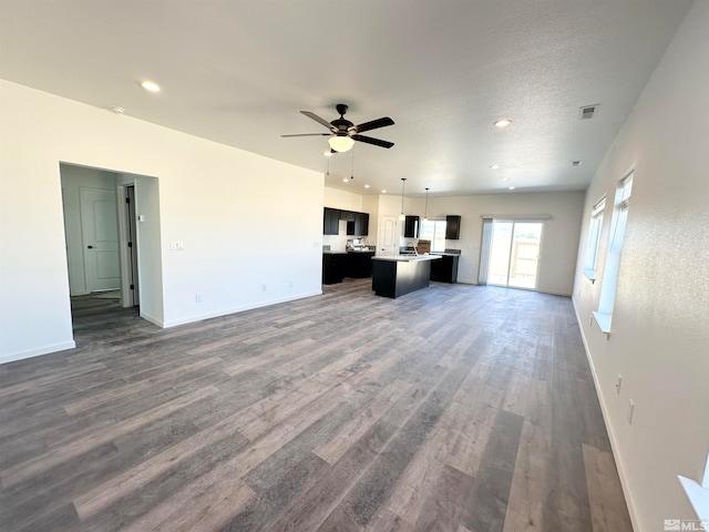 unfurnished living room with a textured ceiling, ceiling fan, and dark wood-type flooring