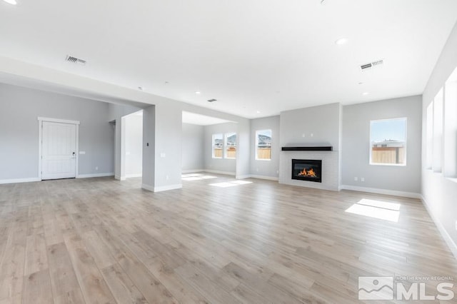 unfurnished living room featuring light hardwood / wood-style floors and a brick fireplace