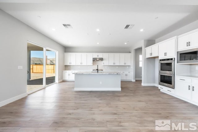 kitchen with a center island with sink, sink, light hardwood / wood-style flooring, appliances with stainless steel finishes, and white cabinetry