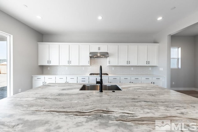 kitchen with decorative backsplash, light stone countertops, white cabinetry, and sink