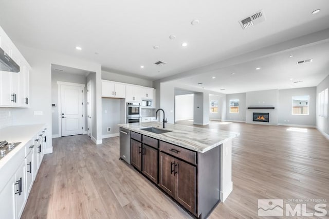 kitchen featuring appliances with stainless steel finishes, light stone counters, dark brown cabinets, sink, and light hardwood / wood-style floors