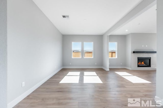 unfurnished living room featuring light wood-type flooring and a brick fireplace