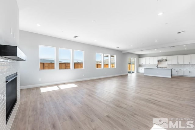 unfurnished living room with light hardwood / wood-style floors and a brick fireplace