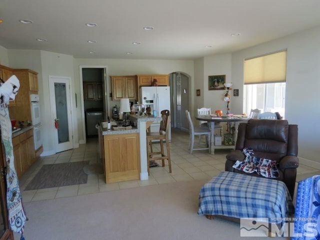 kitchen with a kitchen breakfast bar, white appliances, light tile patterned flooring, and a kitchen island