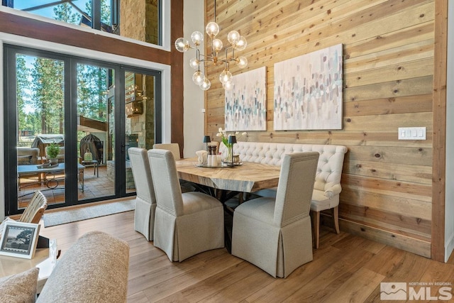 dining space with light hardwood / wood-style flooring, a high ceiling, wood walls, and an inviting chandelier