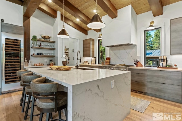 kitchen featuring wood ceiling, an island with sink, light stone countertops, beverage cooler, and sink