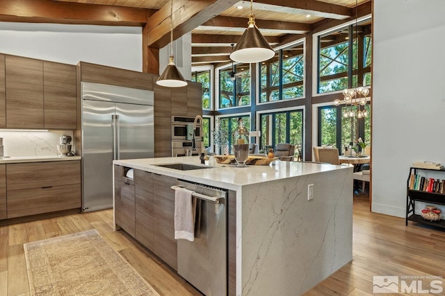 kitchen featuring beamed ceiling, an island with sink, decorative light fixtures, light hardwood / wood-style flooring, and appliances with stainless steel finishes