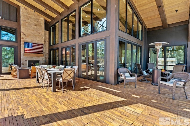 dining area with a stone fireplace, light wood-type flooring, beam ceiling, and high vaulted ceiling