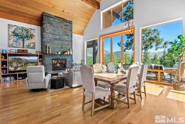 dining room featuring a mountain view, wood ceiling, high vaulted ceiling, a fireplace, and light hardwood / wood-style floors