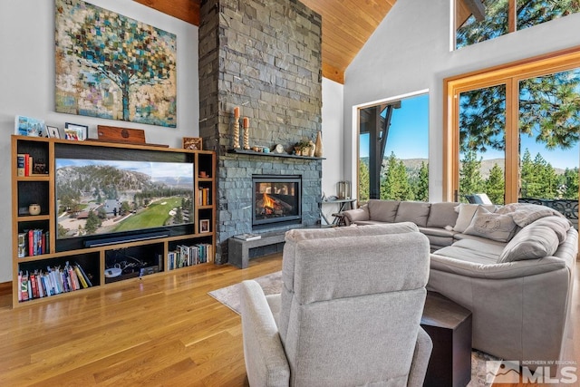 living room with high vaulted ceiling, wood ceiling, hardwood / wood-style flooring, and a stone fireplace