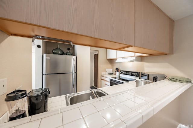 kitchen with sink, tile counters, range with electric stovetop, and stainless steel refrigerator