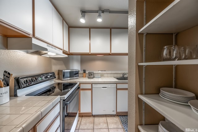 kitchen with track lighting, tile counters, white cabinets, stainless steel appliances, and light tile patterned floors