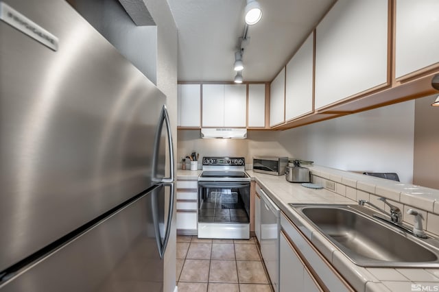 kitchen with light tile patterned flooring, sink, ventilation hood, white cabinetry, and stainless steel appliances