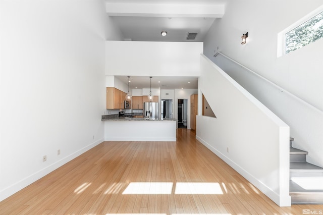 unfurnished living room featuring light wood-type flooring, beam ceiling, and high vaulted ceiling