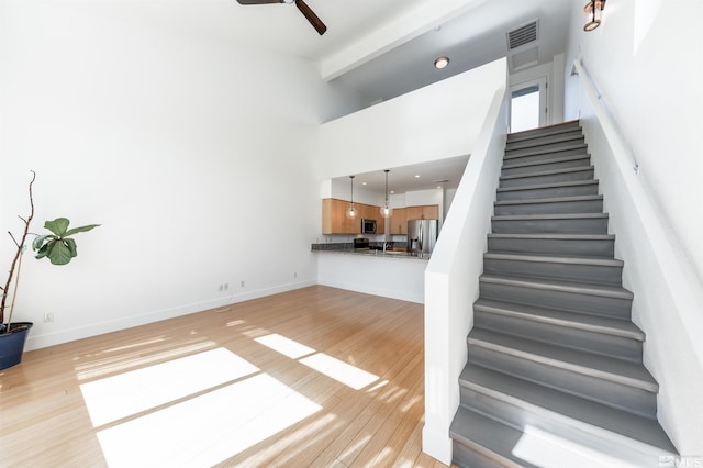 stairway with ceiling fan, beam ceiling, a towering ceiling, and hardwood / wood-style floors