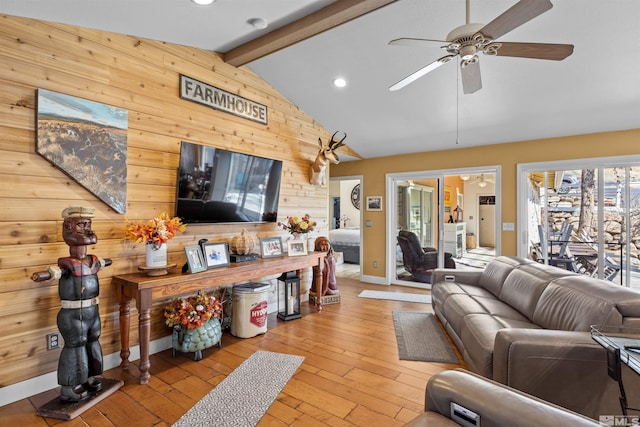 living room with vaulted ceiling with beams, wooden walls, light hardwood / wood-style floors, and ceiling fan