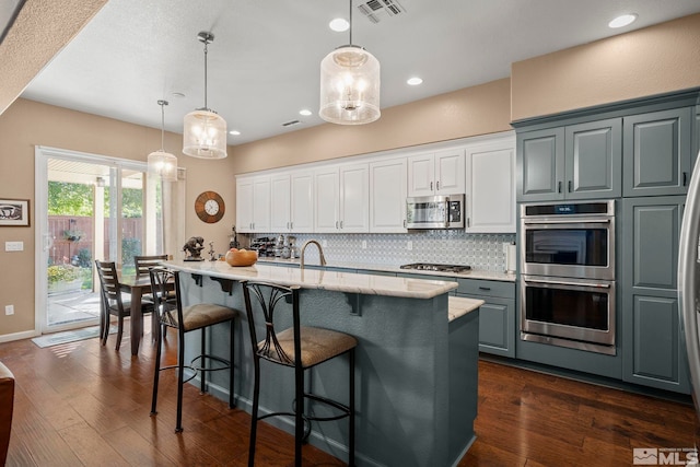 kitchen with an island with sink, hanging light fixtures, white cabinetry, appliances with stainless steel finishes, and dark hardwood / wood-style floors