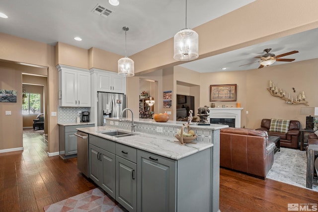 kitchen with gray cabinets, pendant lighting, dark hardwood / wood-style floors, stainless steel fridge with ice dispenser, and a center island with sink