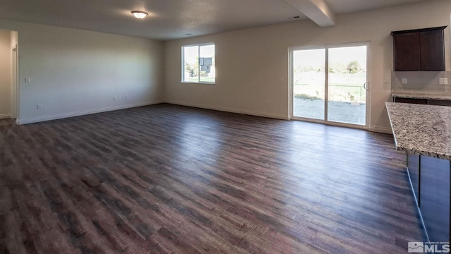 unfurnished living room with beam ceiling, dark hardwood / wood-style flooring, and a healthy amount of sunlight