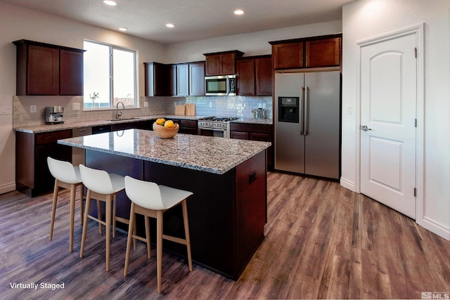 kitchen featuring light stone counters, stainless steel appliances, wood-type flooring, a center island, and sink