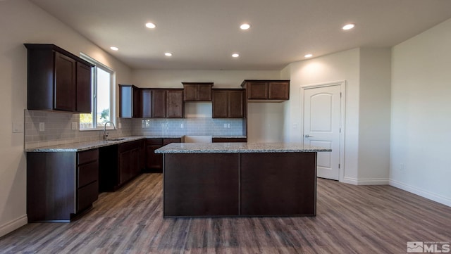 kitchen with wood-type flooring, light stone counters, sink, and a kitchen island