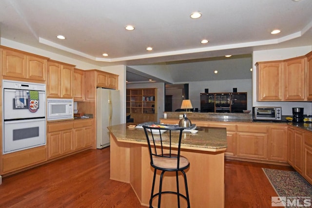 kitchen with a tray ceiling, a center island, dark hardwood / wood-style floors, kitchen peninsula, and white appliances