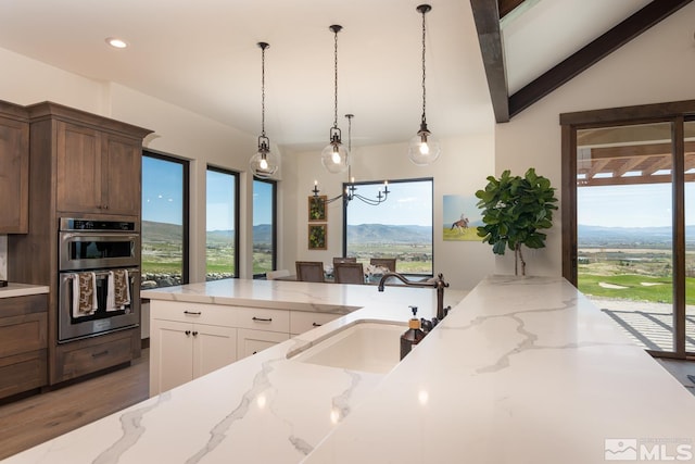 kitchen featuring lofted ceiling with beams, a mountain view, a chandelier, white cabinets, and double oven