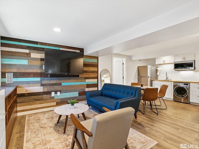 living room featuring light hardwood / wood-style flooring, washer / dryer, and sink