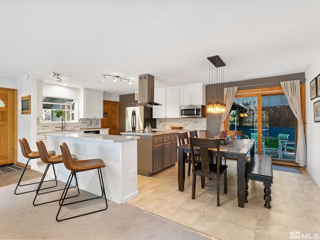 kitchen with pendant lighting, white cabinets, island range hood, a kitchen island, and appliances with stainless steel finishes