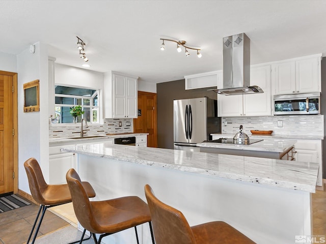 kitchen with white cabinetry, island range hood, decorative backsplash, appliances with stainless steel finishes, and light stone countertops