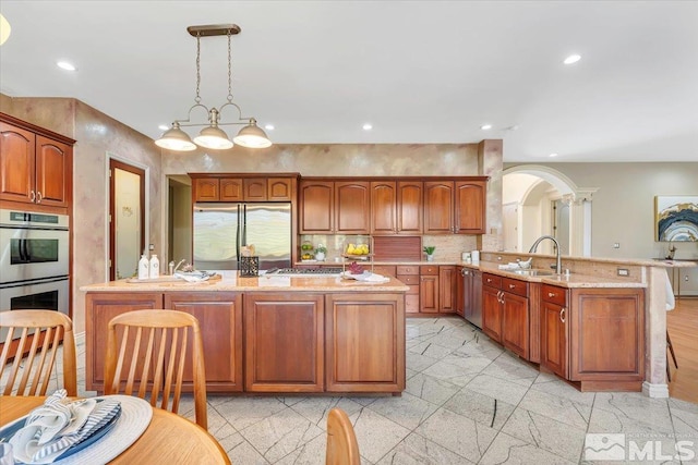 kitchen with sink, kitchen peninsula, stainless steel appliances, decorative light fixtures, and light stone countertops