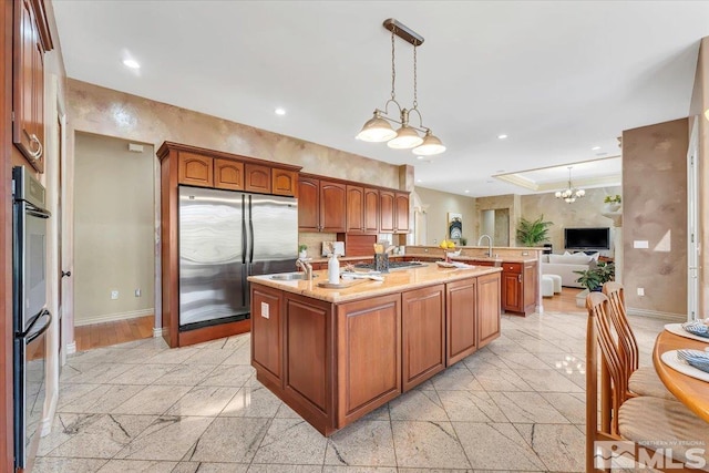 kitchen with light stone counters, an island with sink, a notable chandelier, appliances with stainless steel finishes, and decorative light fixtures