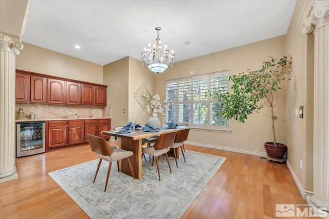 dining space with a notable chandelier, wine cooler, decorative columns, and light hardwood / wood-style floors