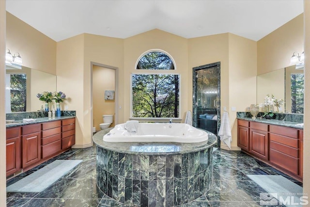 bathroom with a relaxing tiled tub, vanity, and toilet