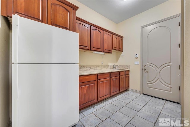 kitchen featuring white refrigerator, light stone countertops, and sink