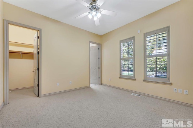 unfurnished bedroom featuring light carpet, a closet, a spacious closet, and ceiling fan