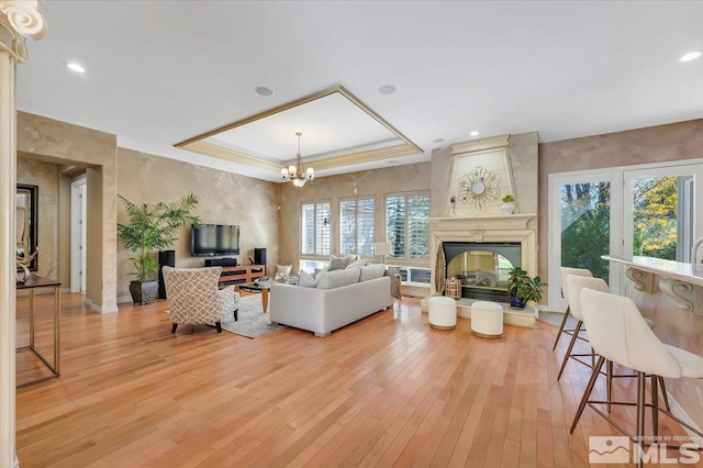 living room featuring a raised ceiling, light hardwood / wood-style floors, a multi sided fireplace, and a wealth of natural light